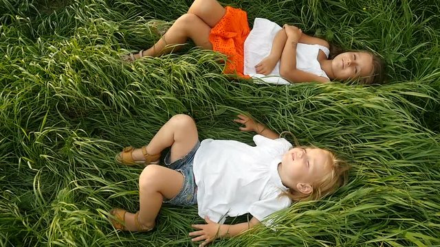 Little girls resting on the green grass. Beautiful kids lying on the field. Cute children dreaming on the nature