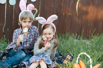 Little girl and boy eat a gingerbread cookie in the shape of the Easter egg.
