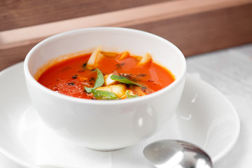 tomato soup with smoked meat in a white bowl on a wooden white background, serving in the restaurant