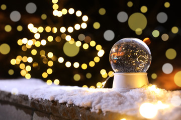 Snow globe and blurred Christmas lights on background, space for text. Winter decor