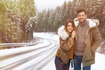 Fototapeta premium Couple walking near snowy forest, space for text. Winter vacation