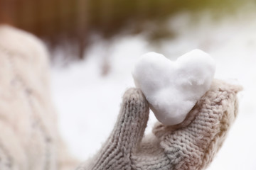 Woman holding heart made of snow outdoors, closeup. Winter day