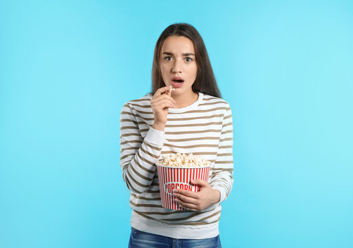 Emotional woman with popcorn during cinema show on color background
