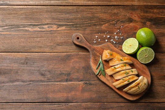 Board with fried chicken breast and limes on wooden background, top view. Space for text