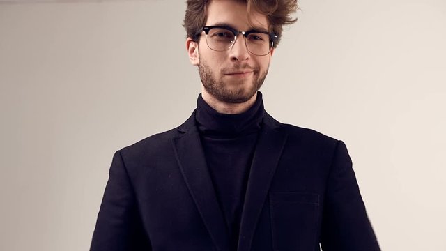 Fashion portrait of handsome elegant man with curly hair wearing suit and glasses on gray background in studio