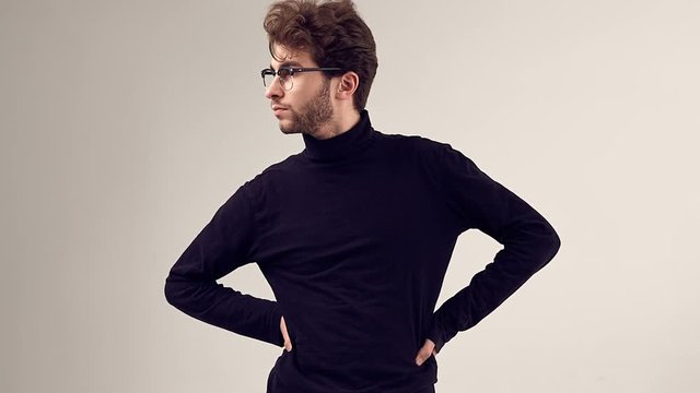 Fashion portrait of handsome elegant man with curly hair wearing black turtleneck and glasses on gray background in studio