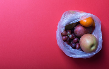 Fruits in plastic bags on a red background with copy space