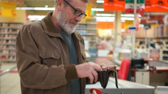 Close portrait of an elderly man with a purse in his hands in the supermarket. Pensioner smiles