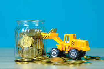 Mini bulldozer truck loading stack coin with pile of gold coin to glass jar, business finance and banking industrial concept.