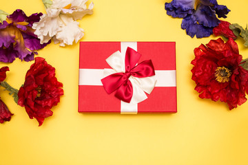 Real box with white and red bow and ribbon with different flowers top view on Valentine's day isolated on yellow background. Flat lay. Copy space.