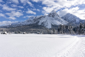 Winter mountain landscape with groomed ski trails and blue sky with white clouds in sunny day. Ehrwald valley, Tirol, Alps, Austria.