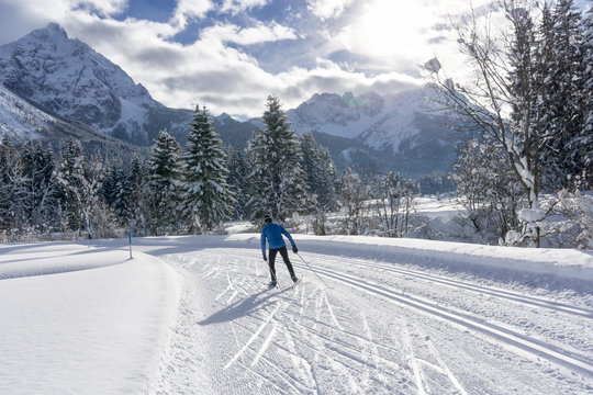 Single cross country skier on groomed ski track, sunny winter day with white clouds on blue sky. Winter mountain landscape, Ehrwald, Tirol, Alps, Austria.
