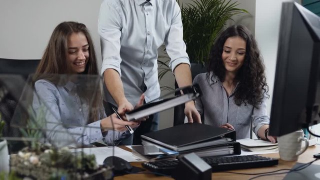 Two beautiful woman working on the project while attractive man bring two document folders.