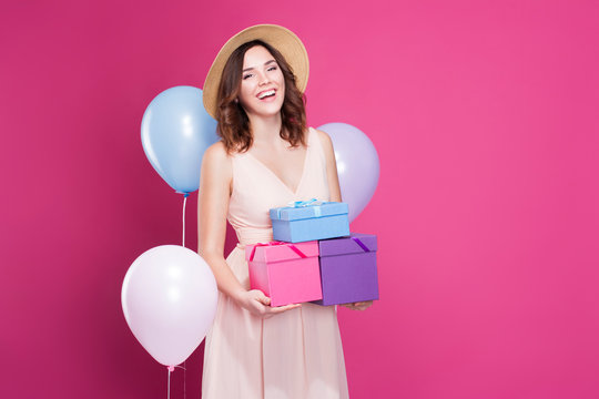 girl in a dress, smiles and holds gifts in her hands, on a pink background