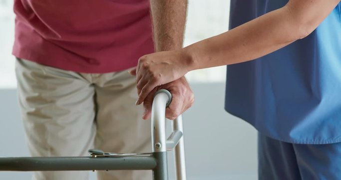 Close up on hand of physical therapist or nurse helping older patient use walker