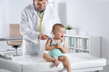 Children's doctor examining little boy with stethoscope in hospital. Space for text