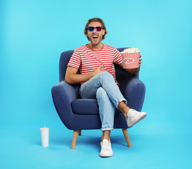 Fototapeta na wymiar Man with 3D glasses, popcorn and beverage sitting in armchair during cinema show on color background