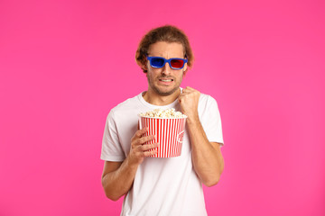 Emotional man with 3D glasses and popcorn during cinema show on color background