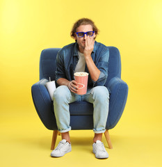 Fototapeta premium Emotional man with 3D glasses, popcorn and beverage sitting in armchair during cinema show on color background