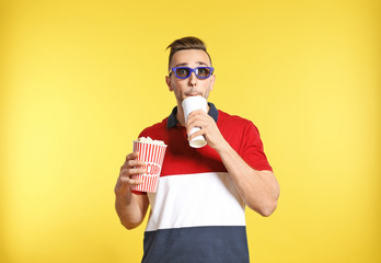 Emotional man with 3D glasses, popcorn and beverage during cinema show on color background