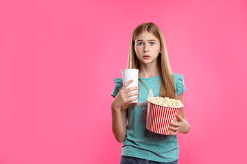 Fototapeta premium Emotional teenage girl with popcorn and beverage during cinema show on color background