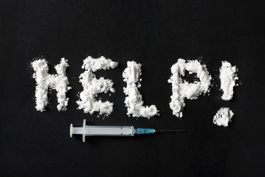 Text Help written with cocaine powder and syringe on black background, top view