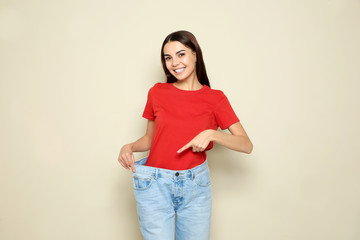 Slim woman in oversized jeans on color background. Weight loss