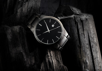 Luxury black metal wristwatch, on top of a pile of coal, with lots of contrast and texture