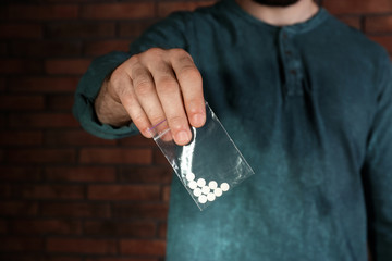 Male dealer holding drugs in plastic bag near brick wall, closeup