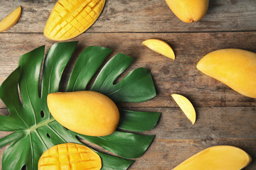 Flat lay composition with mango and tropical leaf on wooden background