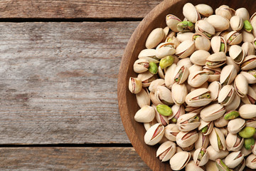 Organic pistachio nuts in bowl on wooden table, top view. Space for text