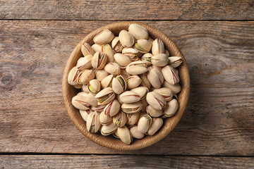 Organic pistachio nuts in bowl on wooden table, top view