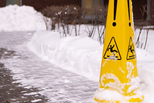 Caution Wet Floor. Slippery Yellow Surface Sign On Red Brick Building And Snow Heap. Slippery Slope. Icing Concept: Be Aware Of Slippery Road And Watch Your Step, Please.