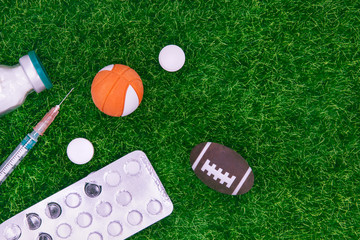 Naklejka premium Medicines, Tablets In Blister, Syringe And Powder For Injection On Background Of Football Or Rugby Ball And Basketball Ball On Blurred Green Grass. Concept Of Doping In American Sports. Copy Space.