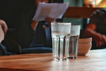 2 Glasses of cold water with ceramic cups in coffee shop on wooden table background, selective focus. Blurred background of pure drinking water in glasses on office desk during meeting, copy space