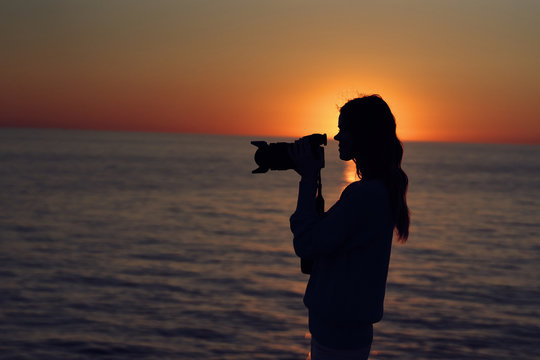 silhouette woman with camera sea sunset
