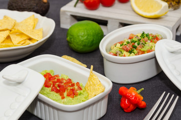 Guacamole and salsa dip next to tortilla chips. A delicious bowl of guacamole next to fresh ingredients on a table with tortilla chips and salsa. 