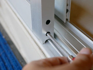 Close up of a screwdriver in a man's hand adjusting sliding glass door rollers