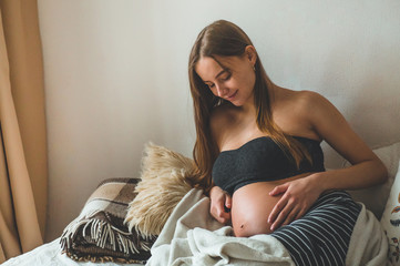 Attractive pregnant woman is sitting in bed and holding her belly. Last months of pregnancy.