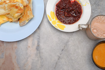 Tea with milk, Roti canai or Roti Parata and curry sauce on the plate over wooden  table