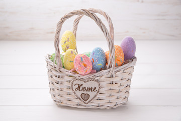Easter eggs in a white basket on a white wooden background