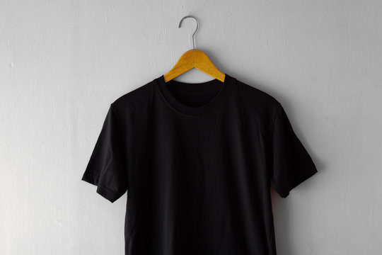 Black t-shirt on wood hanger with grey grunge wall background. Ready for your mock up design or presentation your design project.