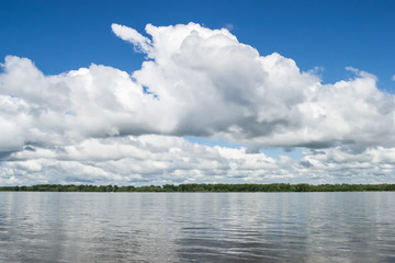 Big white clouds on the blue sky above the river.