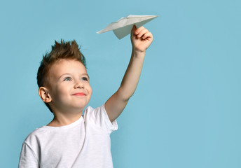 Young baby boy kid in white t-shirt hold paper plane origami smiling looking up on light blue
