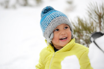 Laughing toddler boy wearing winter clothes in a snow covered mountain.