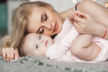 Young pretty mother with her little baby at home. Mom and daughter indoors.  month child with her parent in the bedroom.