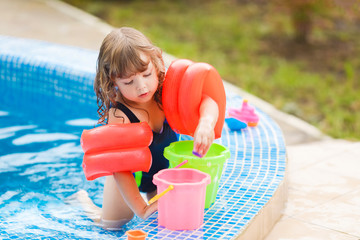 Adorable little girl with inflatable over-sleeves floats sitting in the swimming pool