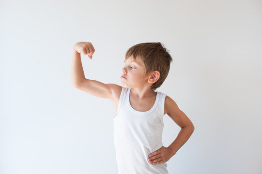 strong small child in white tank top showing his muscle with grimace on his face