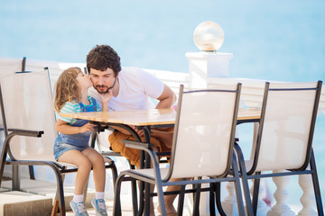 Father and daughter sitting at the outdoors restaurant, sea at the background