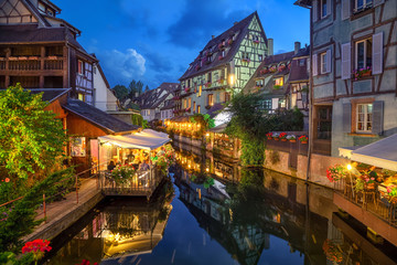 Colmar, France. Half-timbered houses and verandas of restaurants reflecting in the water at dusk in...